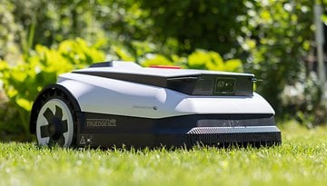 Ecovacs Goat A1600 RTK robotic lawn mower on grass with greenery in the background.